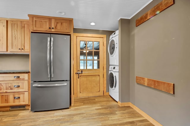 kitchen featuring baseboards, visible vents, light wood-style flooring, stacked washer / drying machine, and freestanding refrigerator