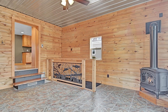 living area with wood walls, a wood stove, and a ceiling fan