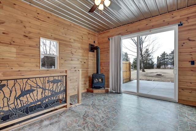 living area featuring a ceiling fan, wood ceiling, a wood stove, stone finish flooring, and wooden walls