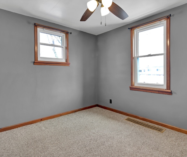 carpeted spare room with baseboards, visible vents, and a ceiling fan