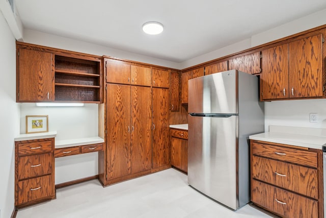 kitchen featuring brown cabinets, freestanding refrigerator, built in study area, and open shelves