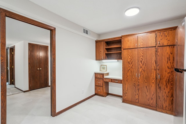 unfurnished office featuring light floors, built in desk, visible vents, and baseboards