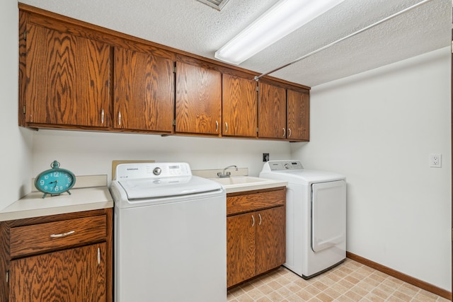 washroom featuring cabinet space, baseboards, a textured ceiling, washing machine and dryer, and a sink