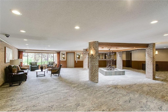 unfurnished living room with a textured ceiling, light colored carpet, a wainscoted wall, wood walls, and ornate columns