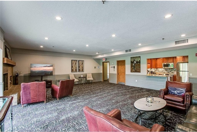 living room featuring a textured ceiling, a fireplace, visible vents, wainscoting, and carpet