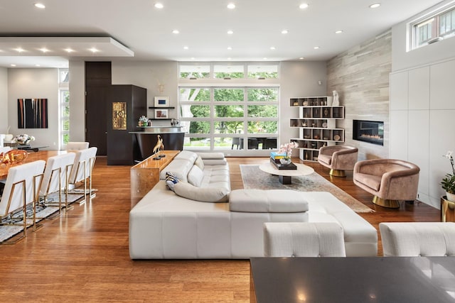 living room featuring recessed lighting, a fireplace, a towering ceiling, and wood finished floors