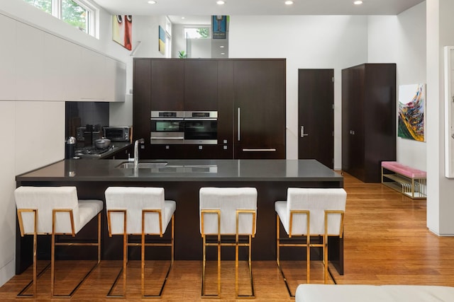 kitchen featuring dark countertops, light wood-style flooring, a breakfast bar area, a peninsula, and a sink