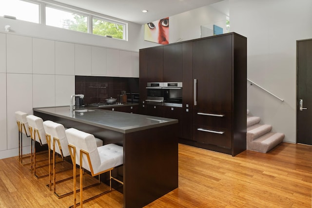 kitchen with a breakfast bar, light wood finished floors, stainless steel appliances, dark countertops, and a peninsula