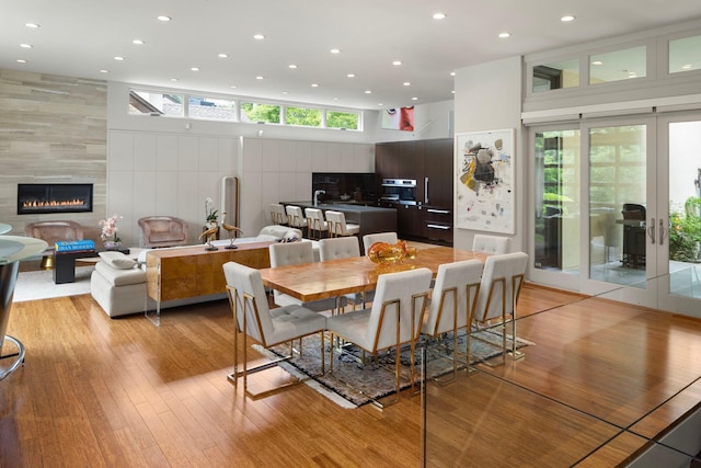 dining space with light wood finished floors, a tiled fireplace, a towering ceiling, and recessed lighting