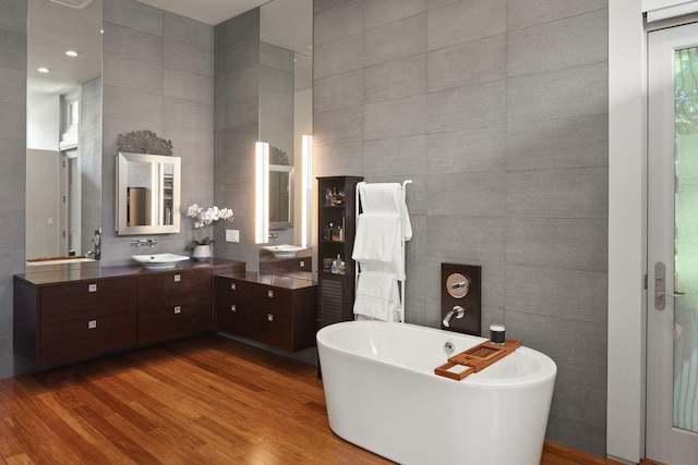 full bathroom featuring a soaking tub, wood finished floors, tile walls, and vanity