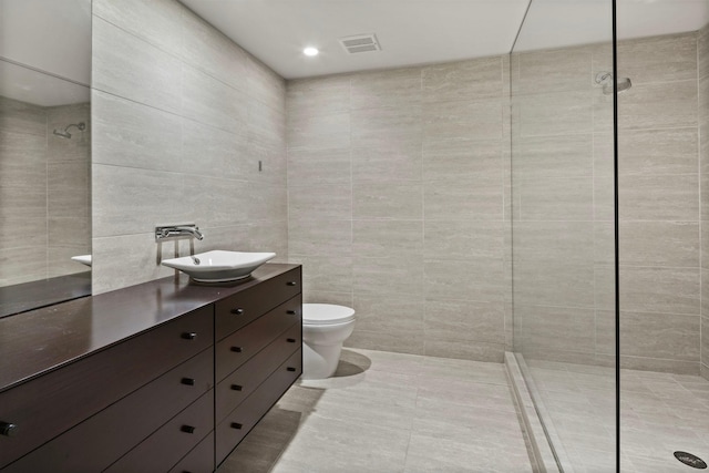 full bathroom featuring visible vents, tiled shower, toilet, vanity, and tile walls