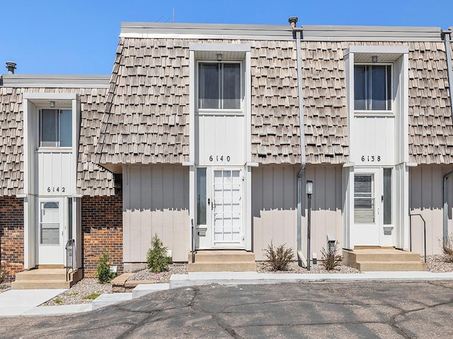 view of front of house featuring brick siding, board and batten siding, and mansard roof
