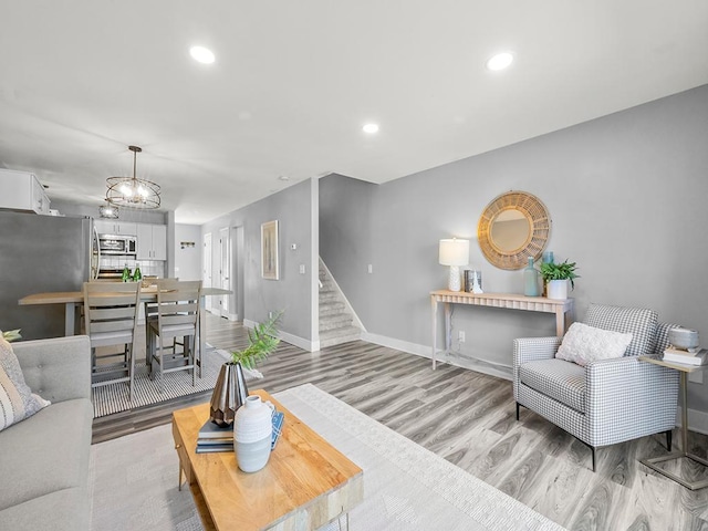living area with light wood-style floors, baseboards, a chandelier, and stairway