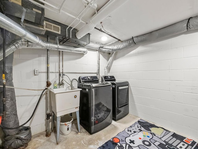laundry area featuring laundry area, visible vents, washing machine and clothes dryer, a sink, and concrete block wall