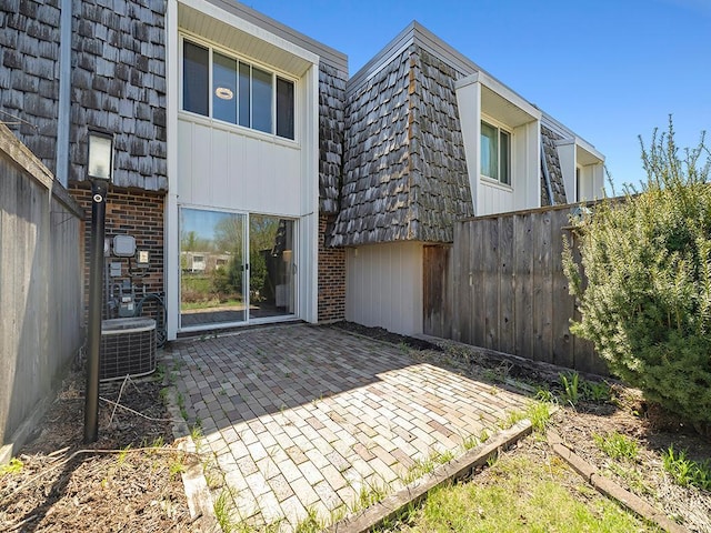 back of house featuring central AC unit, brick siding, mansard roof, fence, and a patio