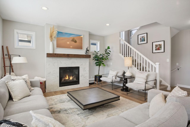 living area featuring a tile fireplace, recessed lighting, wood finished floors, baseboards, and stairs