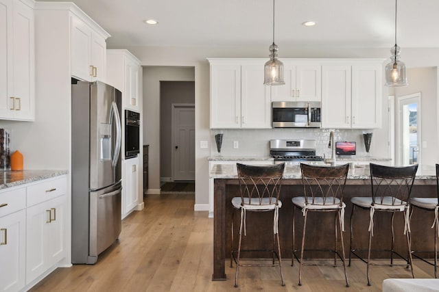 kitchen with appliances with stainless steel finishes, white cabinets, decorative backsplash, and a kitchen breakfast bar