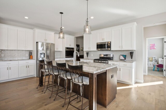 kitchen with stainless steel appliances, white cabinets, light wood-style flooring, and a kitchen breakfast bar