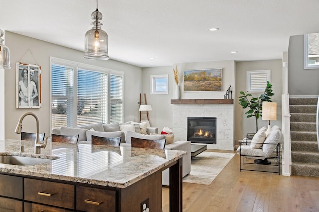 kitchen with decorative light fixtures, a tiled fireplace, a sink, dark brown cabinetry, and light wood-type flooring