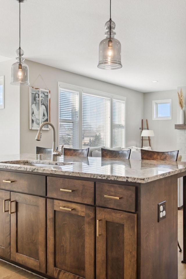 kitchen with pendant lighting, a sink, a kitchen breakfast bar, and light stone countertops