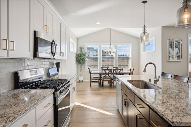 kitchen featuring stainless steel appliances, a sink, vaulted ceiling, decorative backsplash, and hardwood / wood-style floors