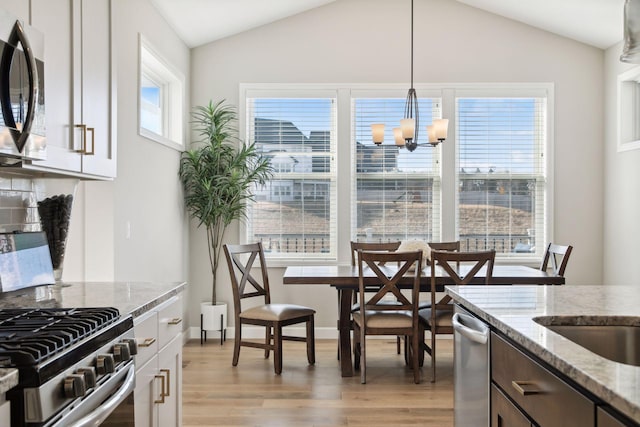 kitchen featuring lofted ceiling, a chandelier, light wood-style flooring, hanging light fixtures, and light stone countertops