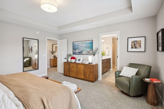 bedroom featuring baseboards, a tray ceiling, ensuite bath, and light colored carpet