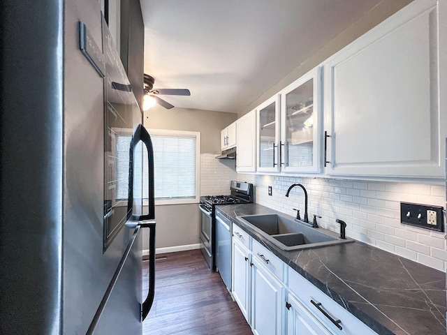 kitchen with dark countertops, appliances with stainless steel finishes, glass insert cabinets, white cabinets, and a sink