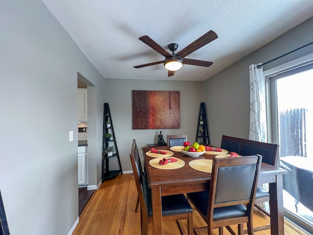 dining area with light wood-type flooring, ceiling fan, baseboards, and a textured ceiling