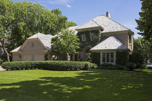 view of front of house featuring an attached garage, a chimney, and a front lawn