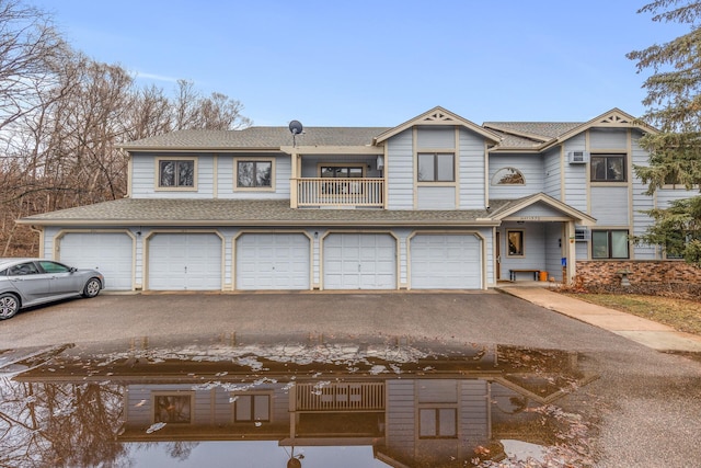 townhome / multi-family property featuring driveway, a balcony, an AC wall unit, and roof with shingles