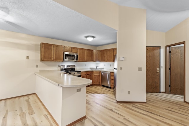 kitchen with stainless steel appliances, a sink, a peninsula, and light wood finished floors