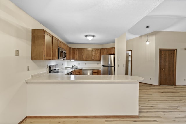 kitchen featuring stainless steel appliances, light countertops, brown cabinetry, light wood-style floors, and a peninsula