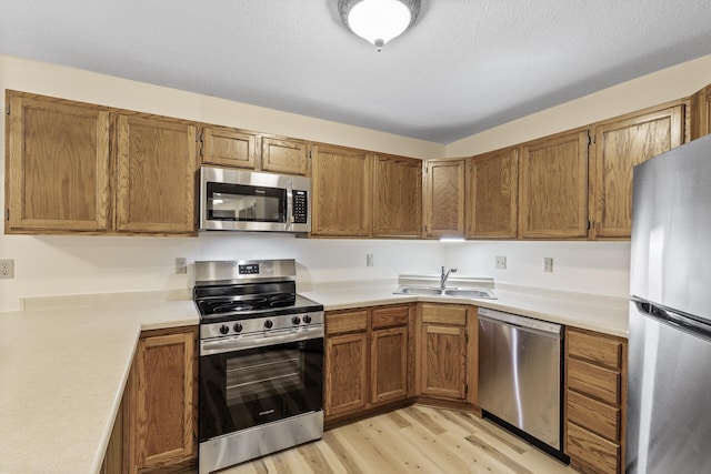 kitchen featuring brown cabinetry, stainless steel appliances, a sink, and light countertops