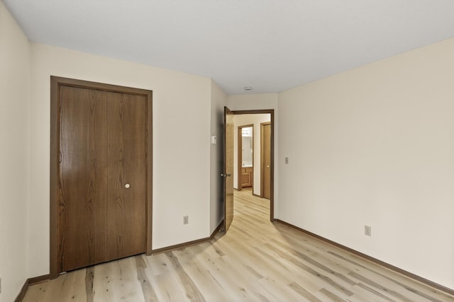 unfurnished bedroom featuring light wood-type flooring, a closet, and baseboards