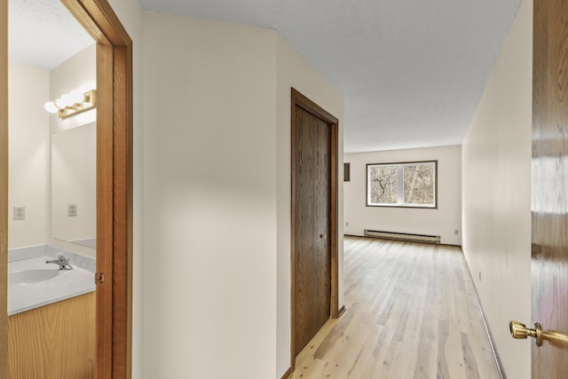 hallway featuring a baseboard heating unit, light wood-type flooring, and a sink