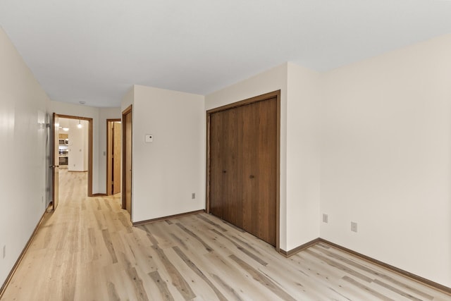 unfurnished bedroom featuring light wood-style floors, baseboards, and a closet