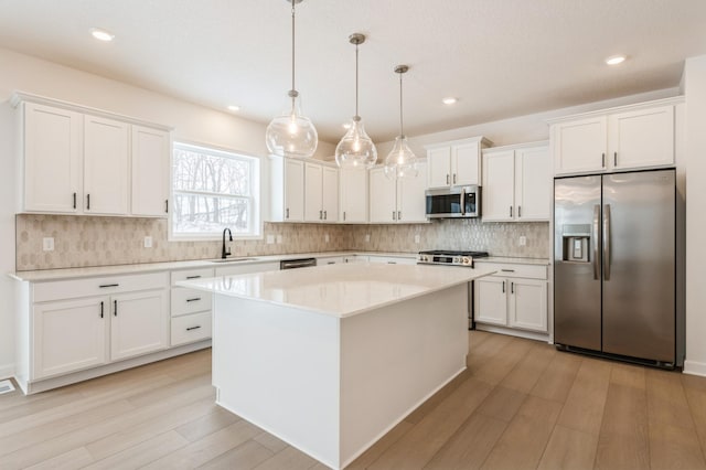 kitchen with appliances with stainless steel finishes, white cabinetry, a sink, and light wood finished floors