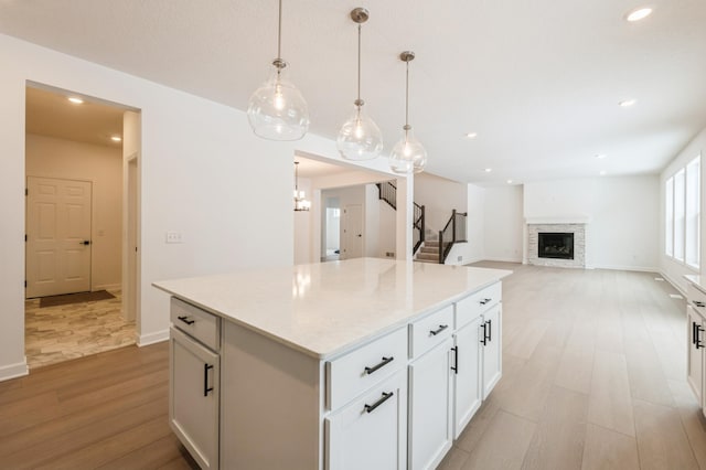 kitchen featuring white cabinets, light wood-style flooring, a center island, a stone fireplace, and recessed lighting