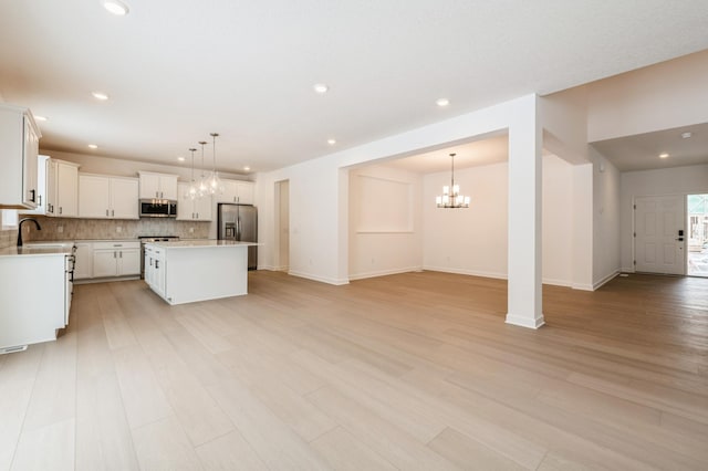 kitchen with open floor plan, appliances with stainless steel finishes, light wood-style flooring, and tasteful backsplash