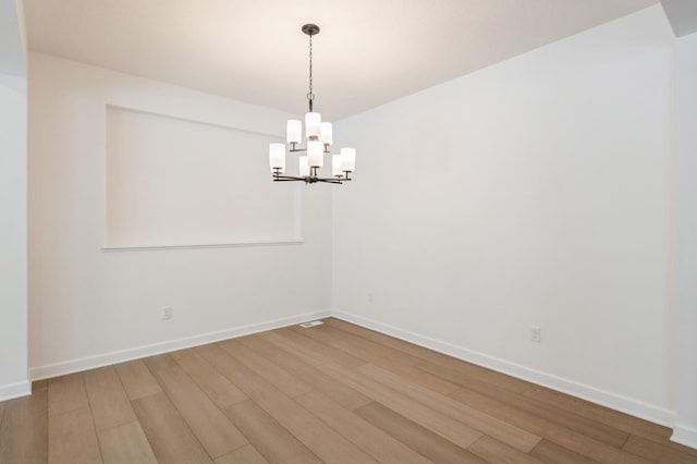 empty room featuring a notable chandelier, baseboards, and wood finished floors