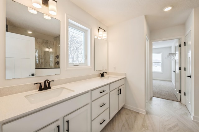 bathroom with marble finish floor, double vanity, a sink, and a walk in shower