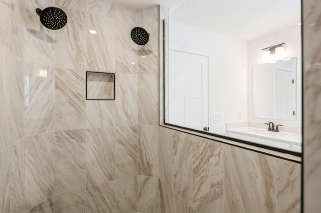 full bathroom with a textured ceiling, tiled shower, and vanity