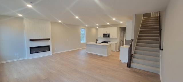 unfurnished living room featuring stairs, a large fireplace, light wood-type flooring, and recessed lighting