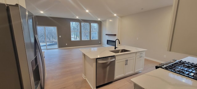 kitchen with white cabinets, appliances with stainless steel finishes, open floor plan, light wood-type flooring, and a sink