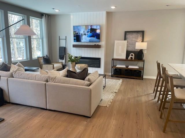 living area featuring recessed lighting, a large fireplace, light wood-style flooring, and baseboards