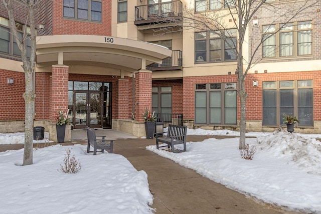 snow covered property entrance featuring french doors, brick siding, and stucco siding