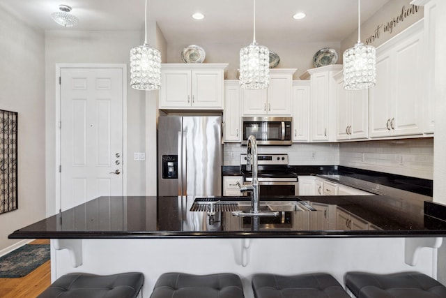 kitchen with a breakfast bar, a peninsula, stainless steel appliances, white cabinetry, and backsplash