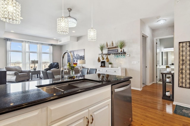 kitchen with light wood finished floors, baseboards, decorative light fixtures, dishwasher, and a sink