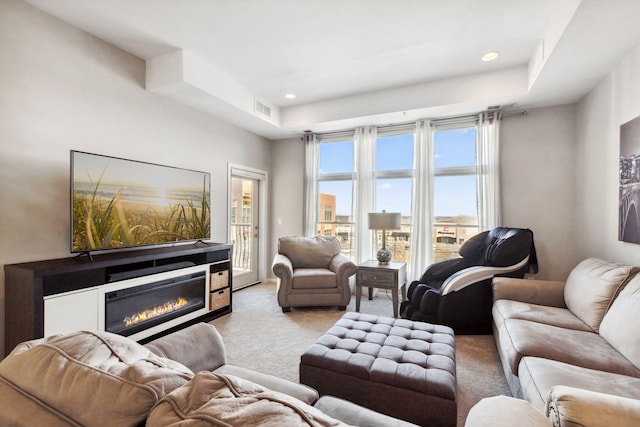 carpeted living room with a glass covered fireplace, a tray ceiling, recessed lighting, and visible vents